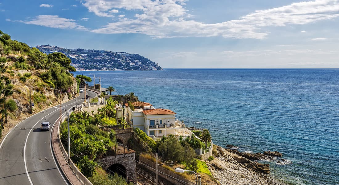 Itinerari-per-viaggi-in-moto-in-Liguria Panoramica strada costiera con curve sinuose, mare azzurro e orizzonte infinito, perfetta per un viaggio in moto indimenticabile.