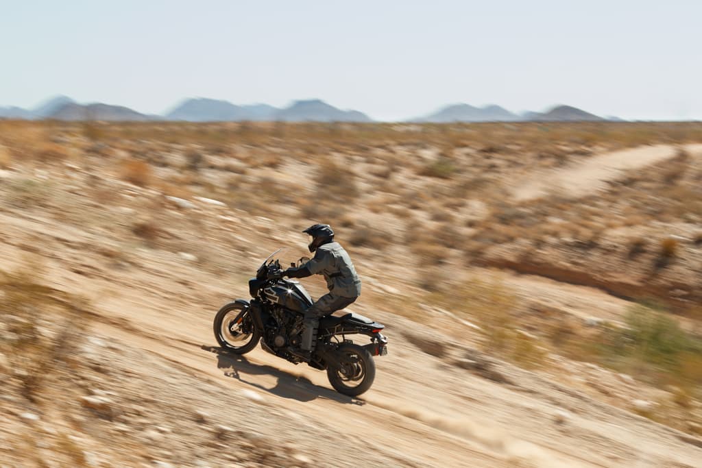 PA3.jpg Pilota con abbigliamento tecnico su moto Harley-Davidson Pan America in test ride off-road su terreno desertico, motori in azione.