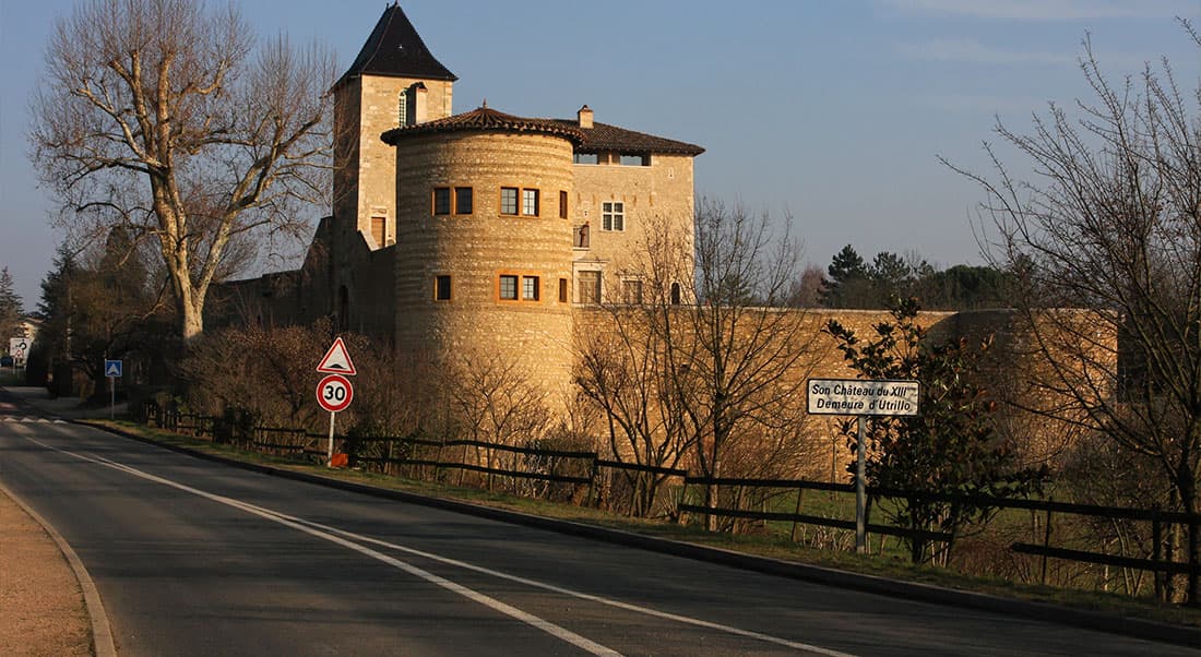 San-Bernardo Castello storico francese del XIII secolo, dimora di Utrillo, con torre e mura in pietra, affiancato da una strada con segnaletica stradale.