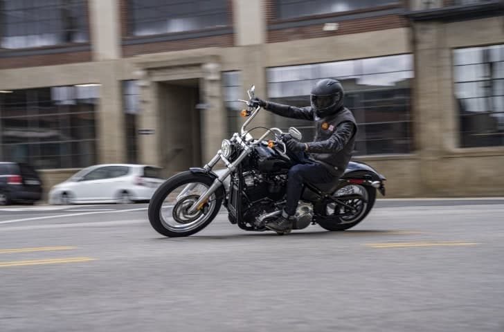 Softail-Standard.jpg Motociclista con casco e abbigliamento tecnico guida una Harley-Davidson nera su strada urbana. Ideale per test ride.