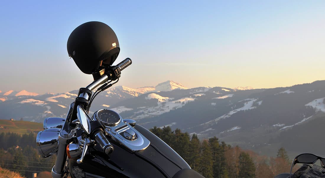 casco-harley Harley-Davidson con casco nero appoggiato sul manubrio, in sosta panoramica su montagne innevate. Pronta per un test ride, esaltando l'esperienza