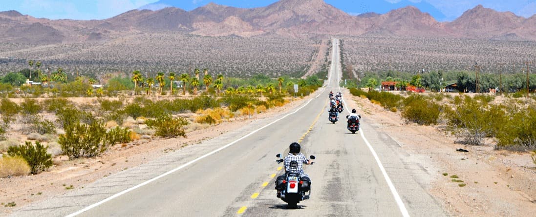 coast-to-coast-in-moto Gruppo di motociclisti su Harley-Davidson in viaggio su una strada desertica. L'abbigliamento tecnico e i motori potenti per un'esperienza unica.