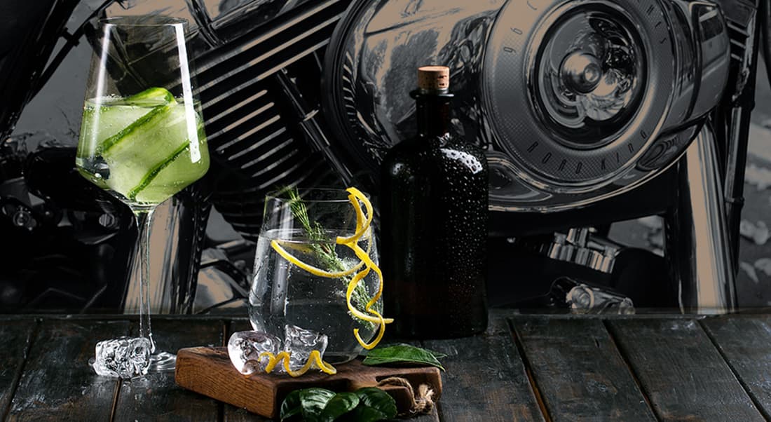 gin-tedesco-The-Archaelogist Cocktail su tavolo in legno scuro con sfondo sfocato di motore e faro cromato di una Harley-Davidson Road King.