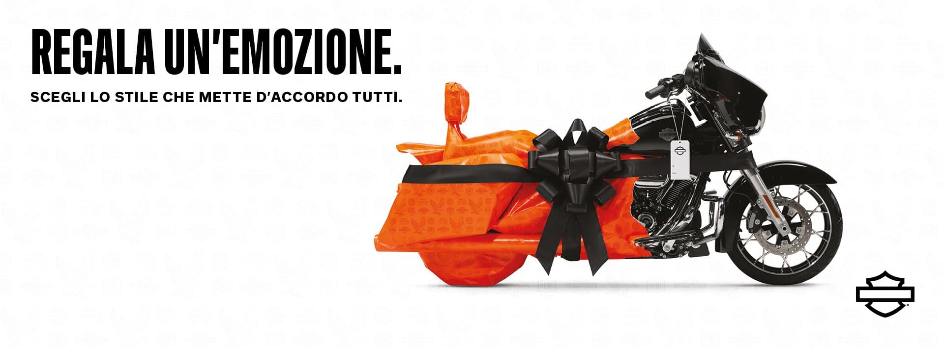 h-d_finalholiday_billboard_1.jpg Harley-Davidson, moto avvolta in carta regalo arancione con fiocco nero, che evoca l'emozione di un regalo unico e lo stile iconico.