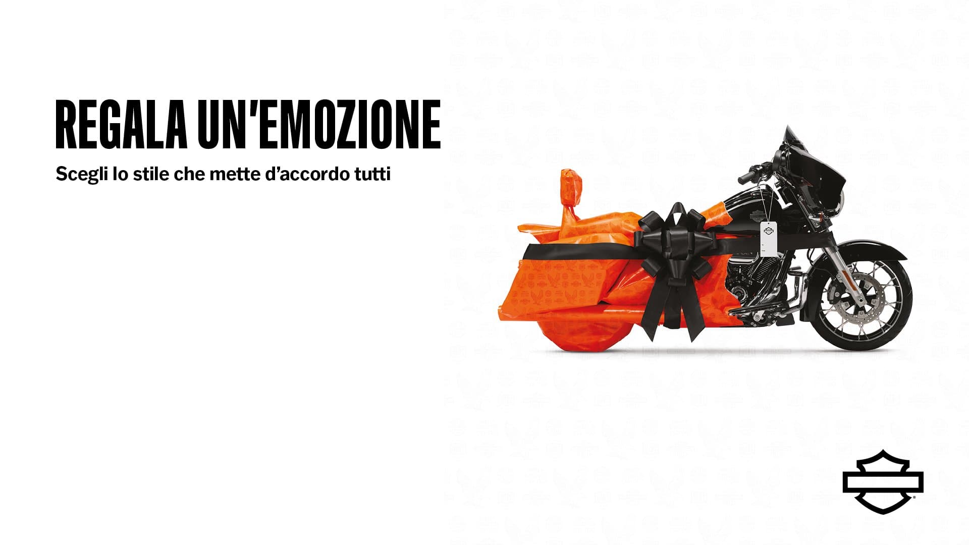 Regala un’emozione Harley-Davidson Motocicletta Harley-Davidson, modello touring, parzialmente avvolta in carta regalo arancione con pattern H-D e fiocco nero. Slogan: REGALA UN'EMOZIONE.