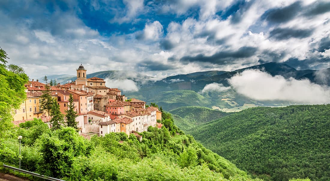 itinerari-in-Umbria Borgo italiano collinare tra montagne nebbiose e valli verdi, evocando percorsi panoramici ideali per moto Harley-Davidson e test ride.