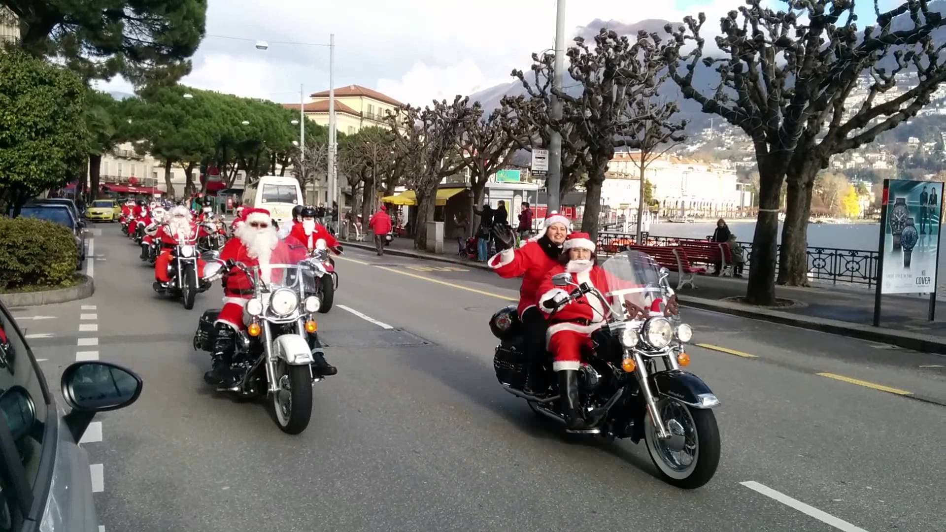 maxresdefault Motociclisti vestiti da Babbo Natale in sella a moto Harley-Davidson, con una passeggera che saluta, durante una parata festiva.