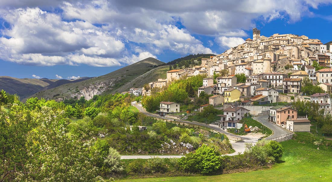 moto-in-Abruzzo Borgo storico italiano arroccato su una collina, con edifici in pietra, torre campanaria, strade tortuose e paesaggio montano verde.