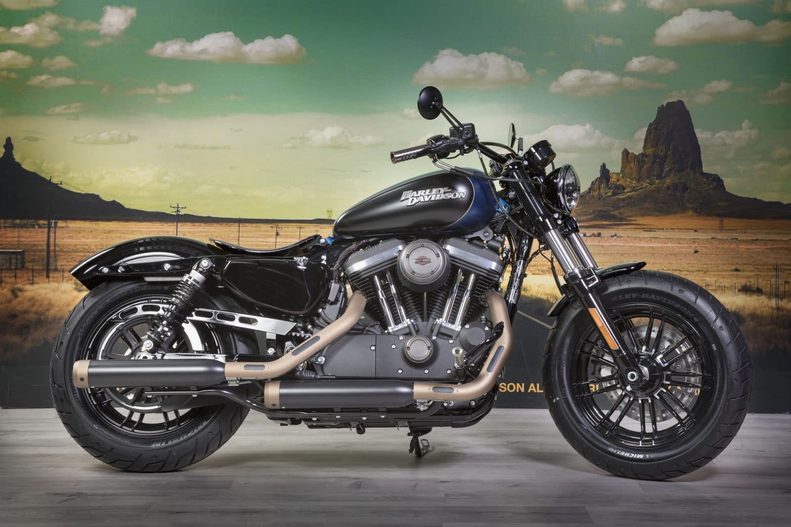 moto-usate Harley-Davidson Sportster Forty-Eight nera opaca con dettagli blu e scarichi color bronzo, esposta in showroom con sfondo desertico.