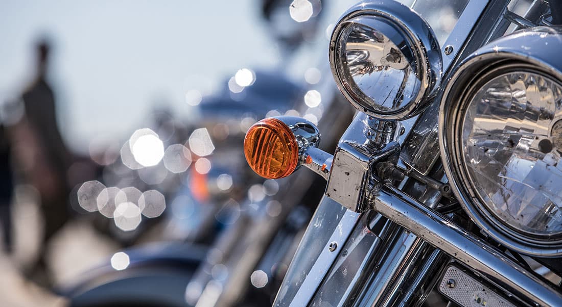 motoraduni-Harley Dettaglio ravvicinato del faro anteriore e dell'indicatore di direzione arancione di una moto Harley-Davidson, con cromature lucide e sfondo sfocato.