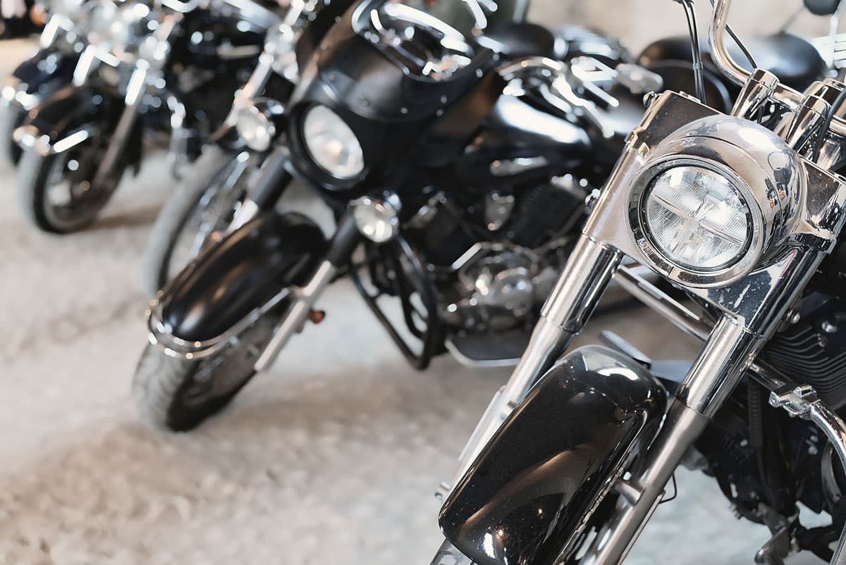 scavino-1-su-3-giugno Dettaglio frontale di motociclette Harley-Davidson cruiser nere e cromate in esposizione, con faro LED e forcella lucida in primo piano.