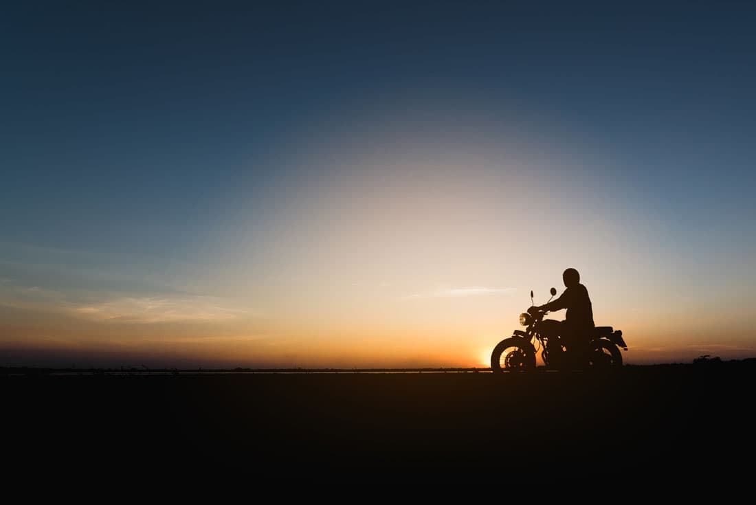 scavino-30-ottobre Motociclista in silhouette su moto al tramonto, cielo sfumato blu e arancione. Evoca libertà e avventura, ideale per test ride Harley-Davidson.