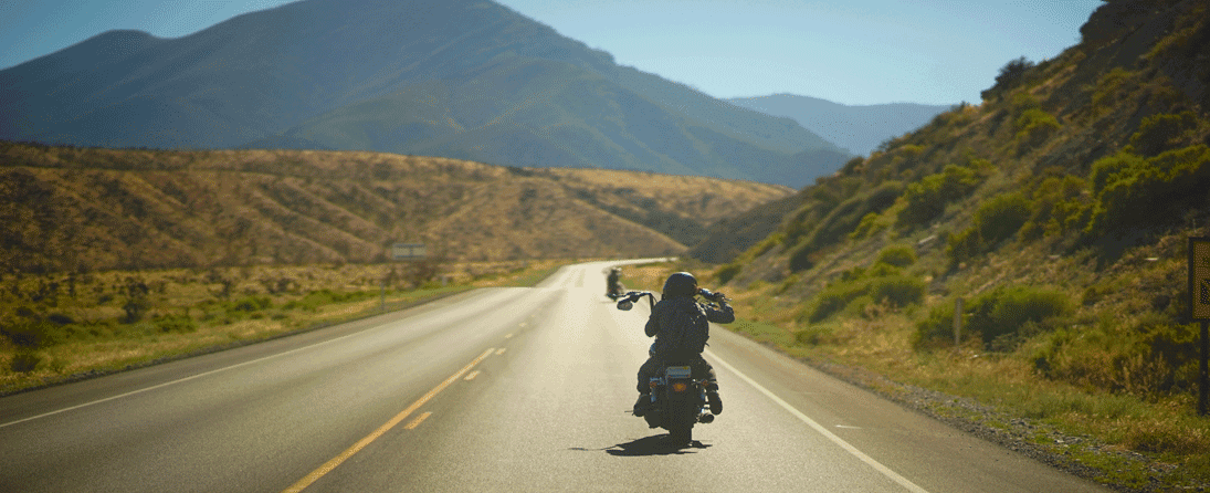 storia-harley Motociclista su Harley-Davidson percorre una strada di montagna assolata, con un'altra moto in lontananza, evocando libertà e avventura.