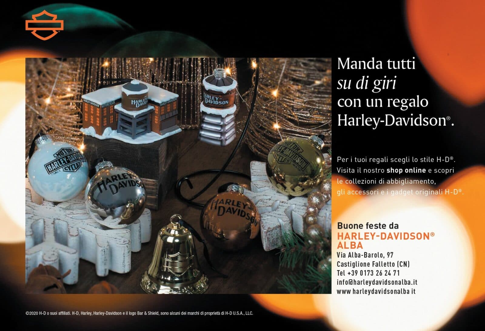 xmas2020_1.jpg Addobbi natalizi Harley-Davidson: palline lucide, campana dorata e miniature di edifici, su sfondo festivo con luci. Promozione regali H-D.