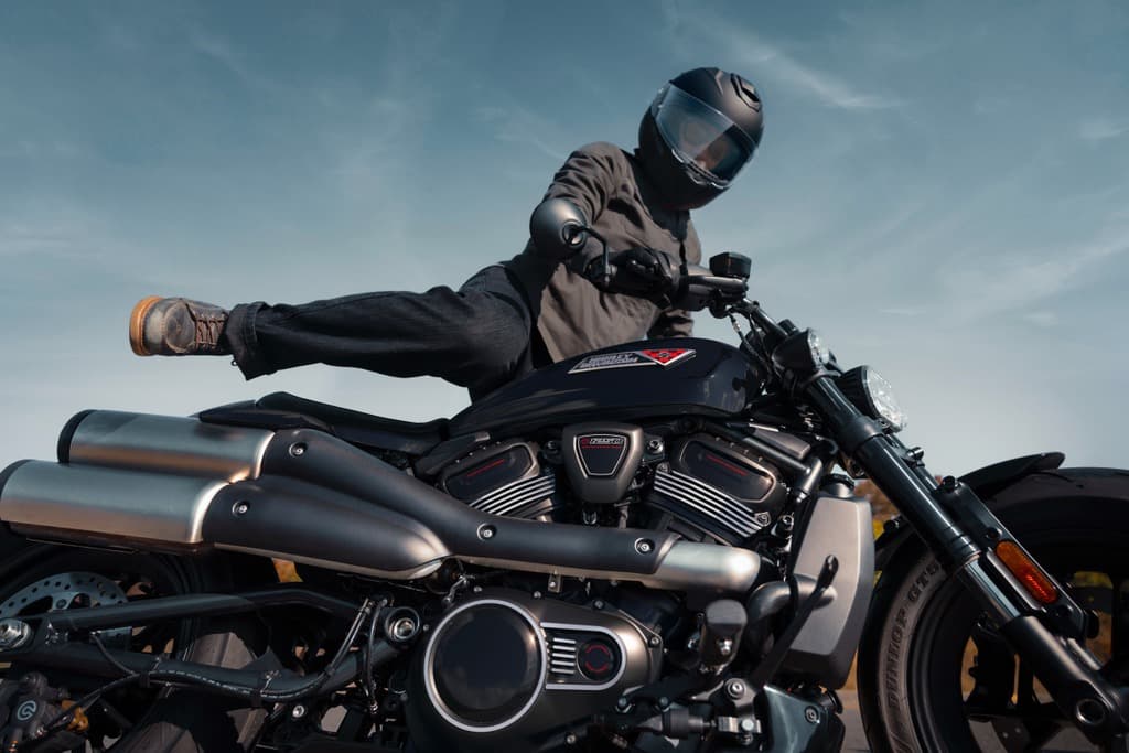 Harley-Davidson: stile e dinamismo in sella. Persona con casco e abbigliamento tecnico in posa acrobatica su una Harley-Davidson con motore Revolution Max 1250T, contro il cielo.