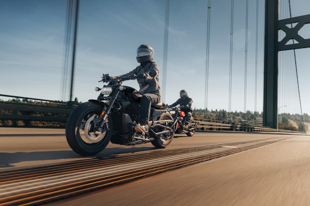 Due Harley-Davidson in viaggio su un ponte Due motociclisti con caschi e abbigliamento tecnico guidano moto Harley-Davidson, una nera e una rossa, su un ponte. L'immagine evoca