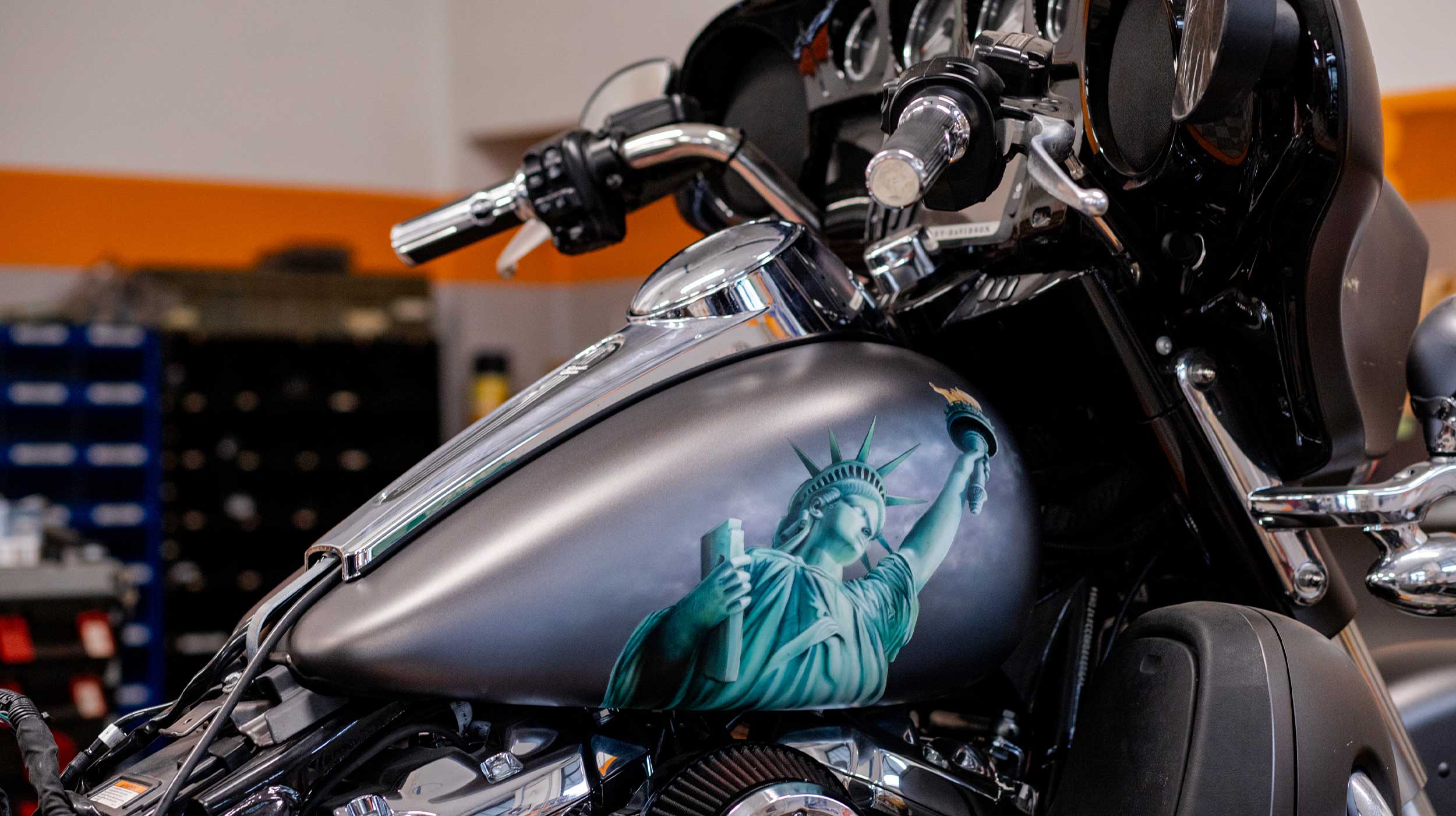 Harley-Davidson customizzata: Statua della Libertà sul serbatoio Serbatoio di una moto Harley-Davidson con aerografia personalizzata della Statua della Libertà, dettagli cromati e manubrio in primo piano.