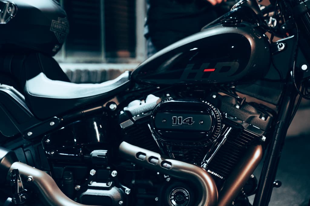 Harley-Davidson 114: potenza e stile. Prenota un test ride ad Alba. Dettaglio laterale di una moto Harley-Davidson scura, evidenziando il serbatoio con logo HD, motore Milwaukee-Eight 114 e scarichi bronzo.