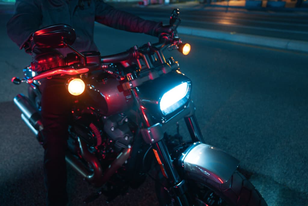 Emozione notturna: test ride su Harley-Davidson moderna. Motociclista con abbigliamento tecnico su Harley-Davidson moderna, faro LED blu e indicatori ambra accesi, in strada di notte.