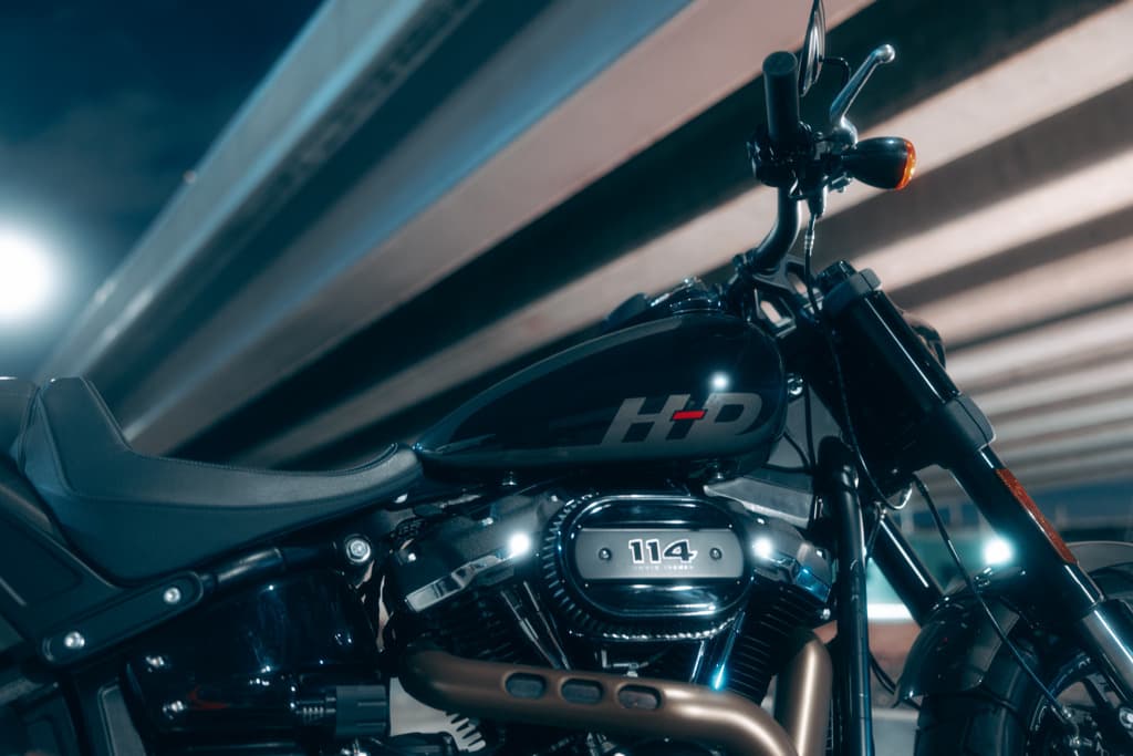 Dettaglio Harley-Davidson 114: potenza e stile moto. Harley-Davidson scura con motore Milwaukee-Eight 114, logo HD sul serbatoio, manubrio e sella in primo piano, sotto una struttura illuminata.