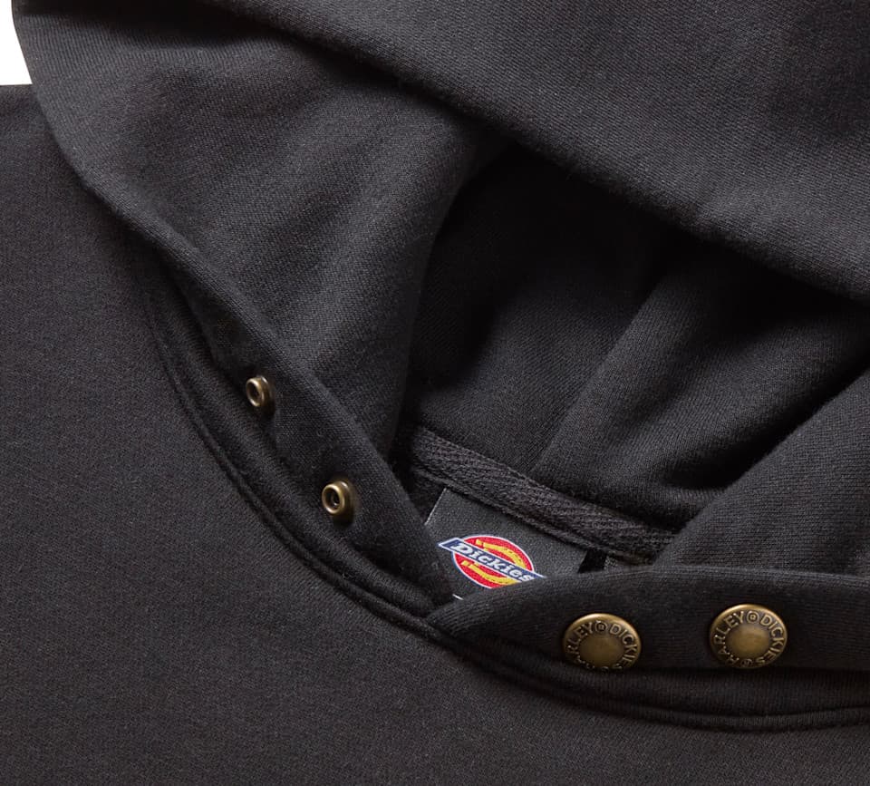 Felpa nera con cappuccio Harley-Davidson x Dickies Dettaglio ravvicinato di una felpa con cappuccio nera, con bottoni a pressione in metallo bronzato. Visibile l'etichetta del brand Dickies e bottoni personalizzati Harley Dickies.