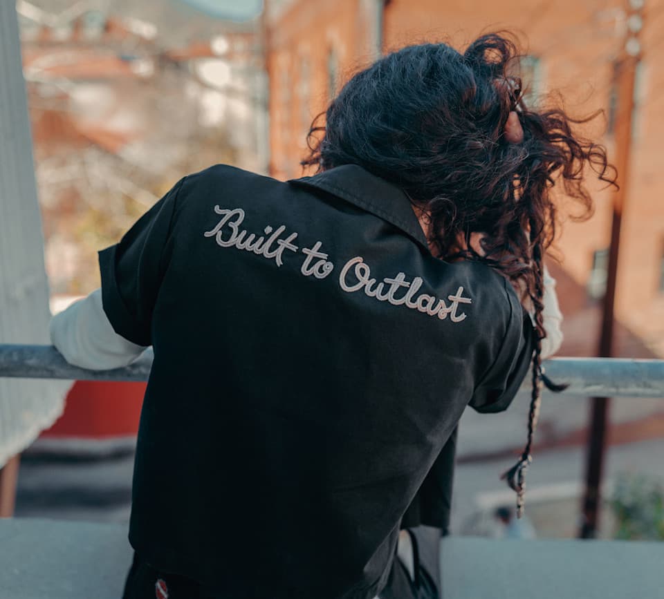 Abbigliamento Harley-Davidson: Built to Outlast Individuo di spalle con camicia nera ricamata 'Built to Outlast', che incarna la robustezza e l'affidabilità dei prodotti Harley-Davidson.